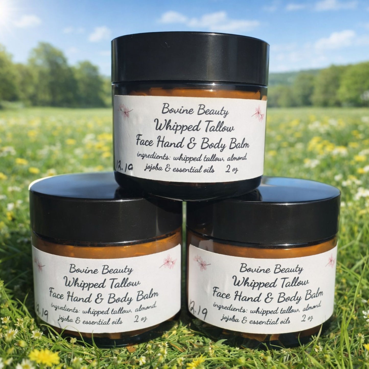 Three jars of Bovine Beauty Whipped Tallow Face Hand & Body Balm on grass with a scenic background