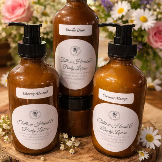 Three bottles of Tallow Hand & Body Lotion with labels on a wooden surface surrounded by flowers.
