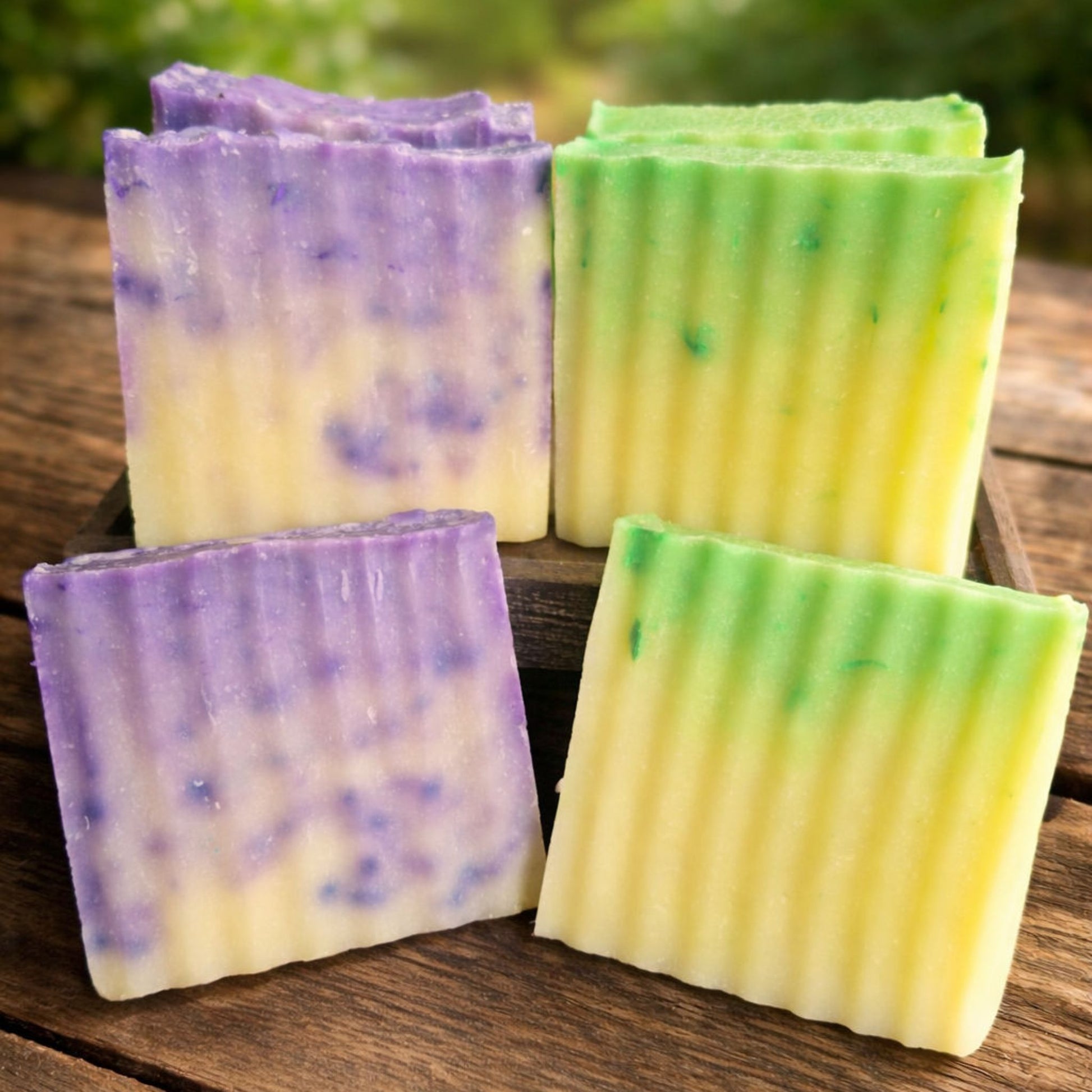 Two stacks of handmade soap bars, one purple and yellow, the other green and yellow, on a wooden surface.