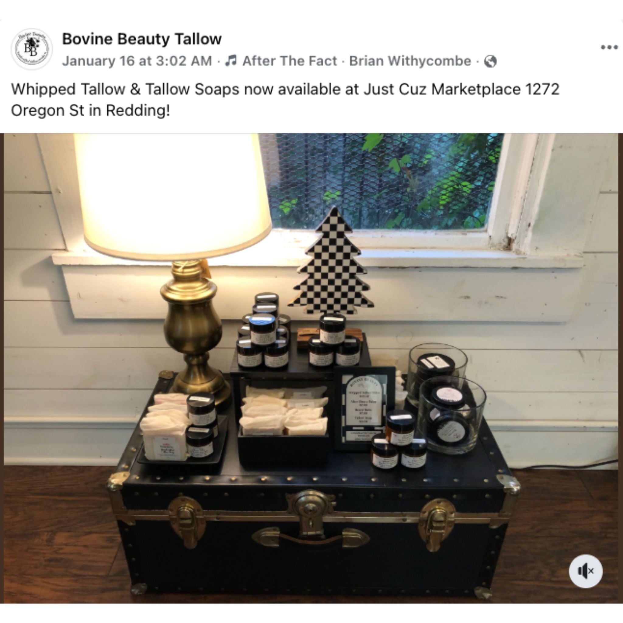 Vintage suitcase with tallow products on a wooden surface, with a lamp and window in the background.